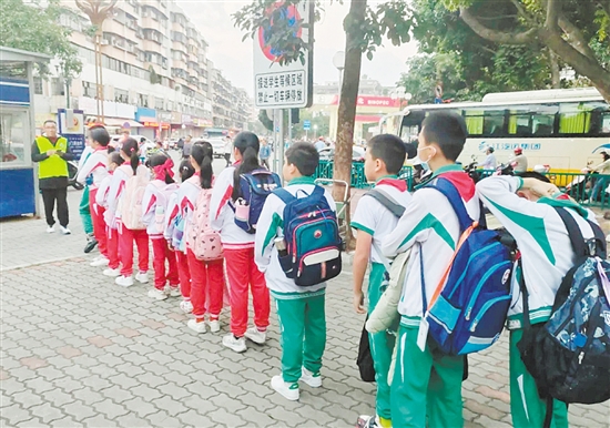 新会圭峰小学的学生们在校园定制公交工作人员的引导下有序排队等待接送。